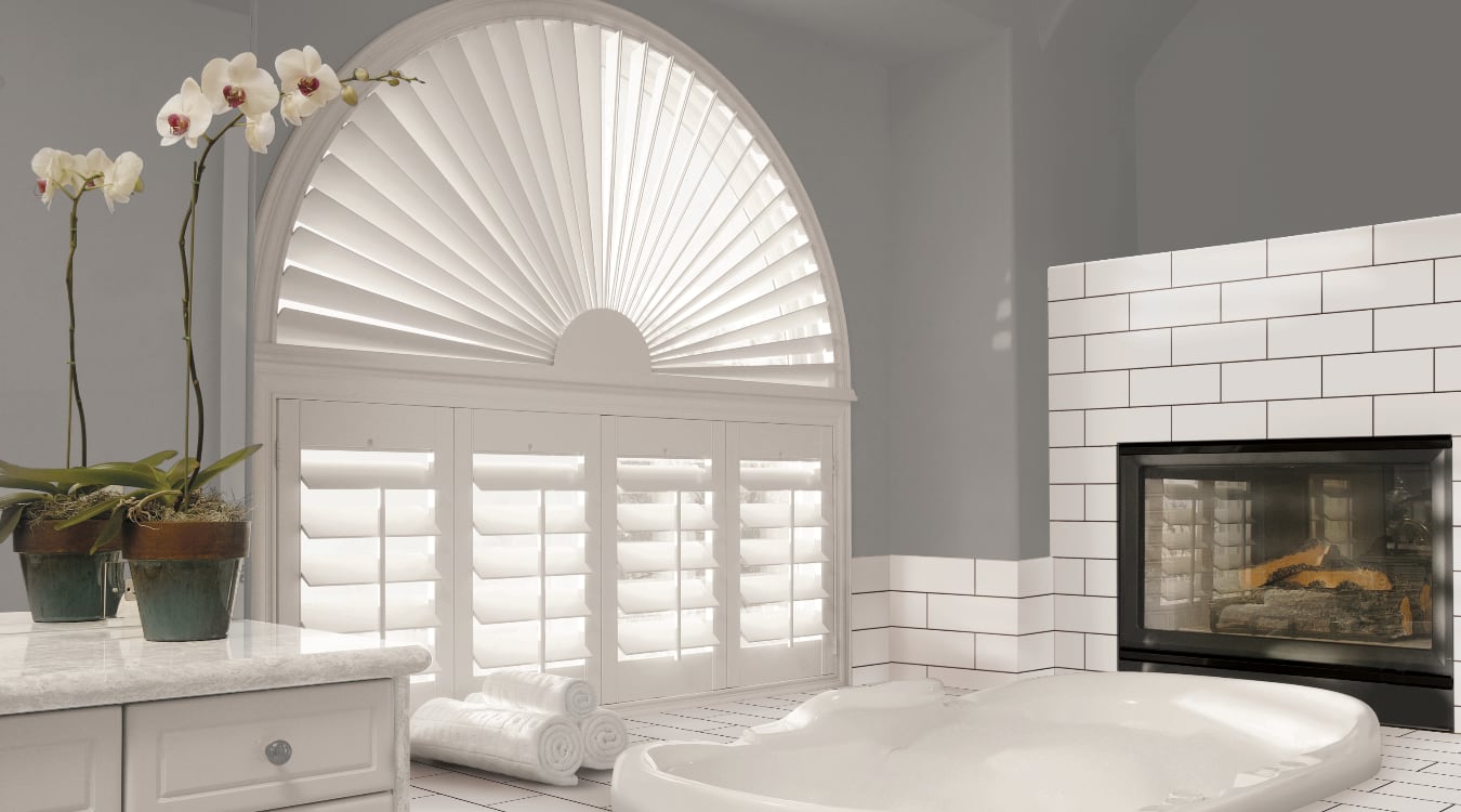 Arched plantation shutters over a tub.